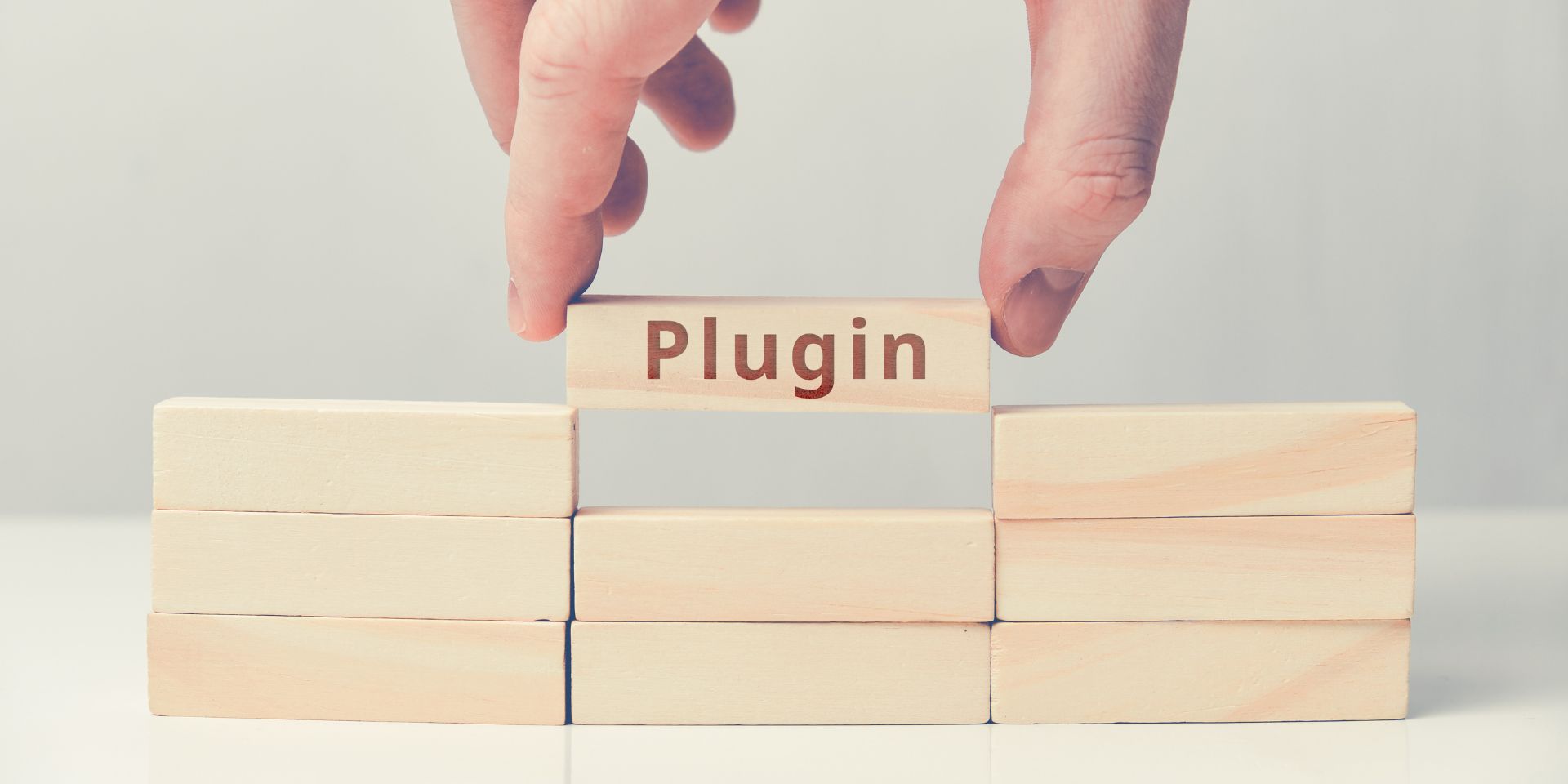 A wooden block with the word 'plugin' is lifted up by a hand.