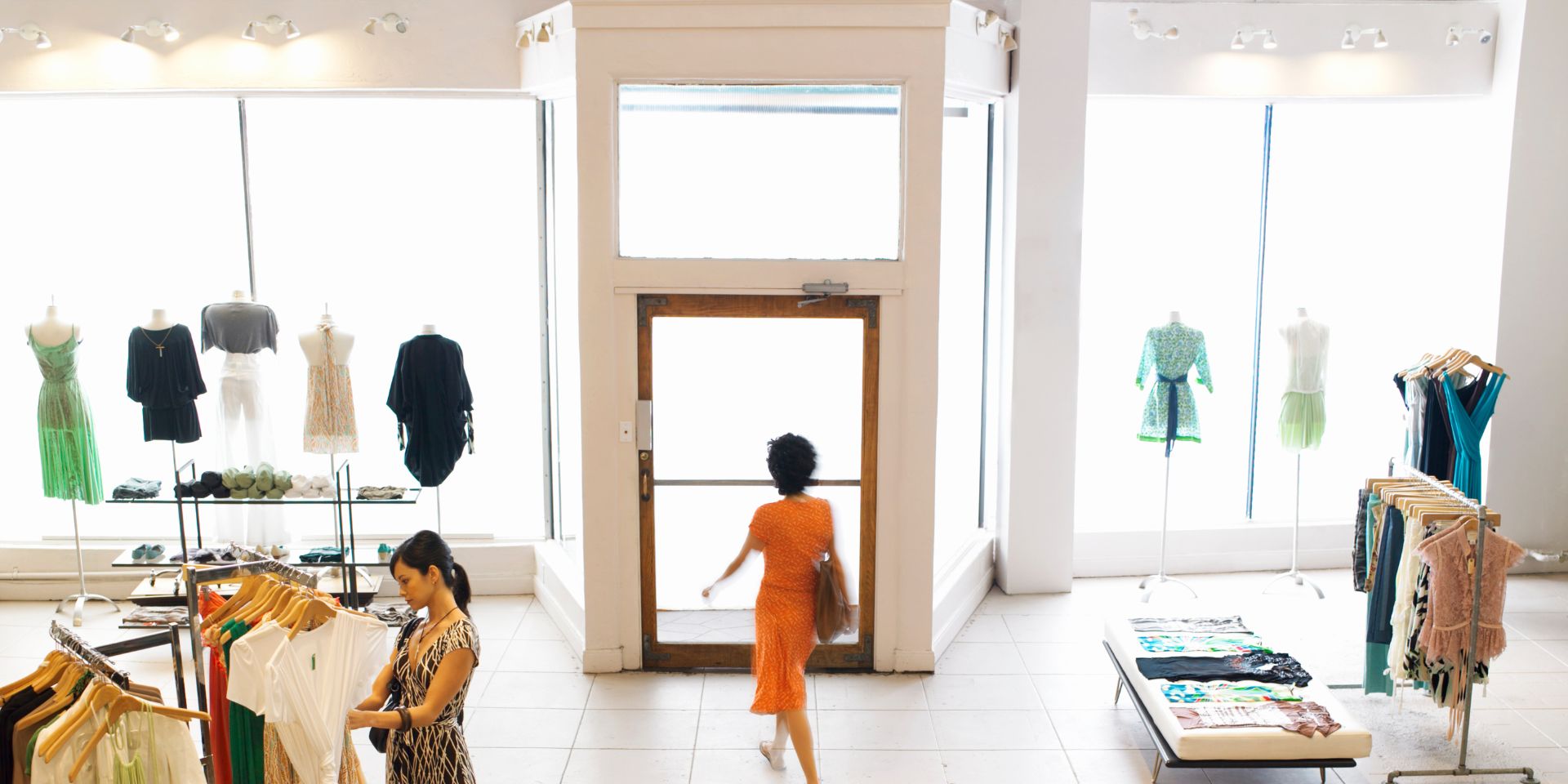 A lady wearing an orange dress leaves a clothes shop.