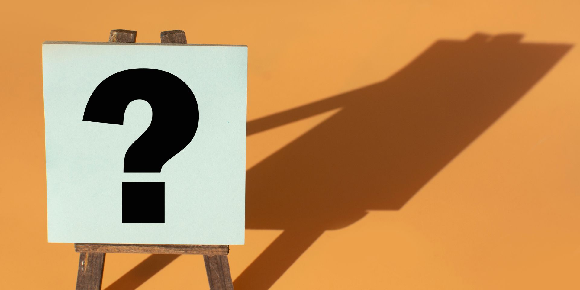 A question mark sign rests on an easel, casting a shadow against a peach background.