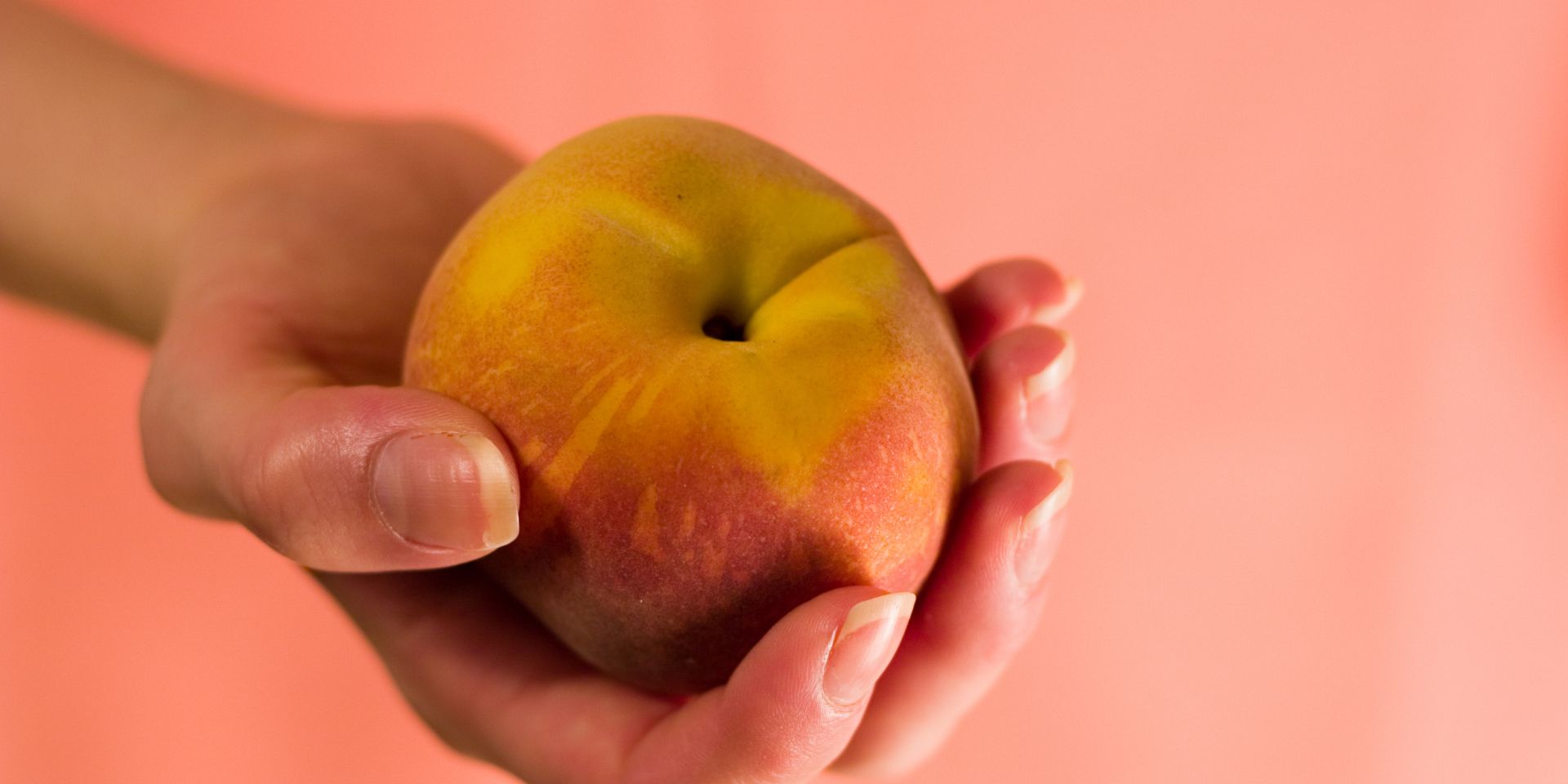 Woman's hand holds out a peach, echoing the Pantone Colour of the Year (Peach Fuzz).